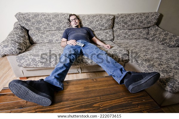 Adult man resting in sofa like a couch potato with\
remote control on belly