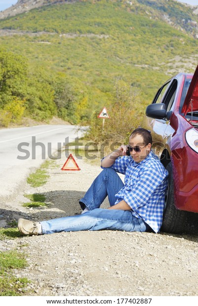 Adult\
man is sitting near his broken car waiting for\
tow