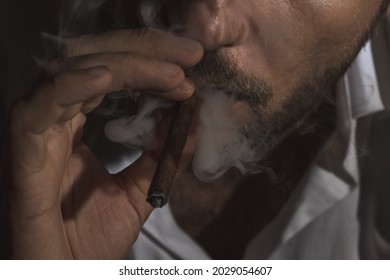 The adult man smoking cigar and blows smoke out of the mouth. 