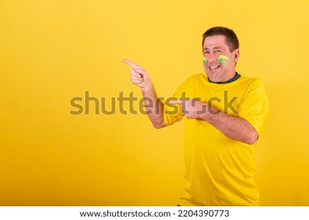 adult man, soccer fan from brazil, pointing with fingers something to his left.