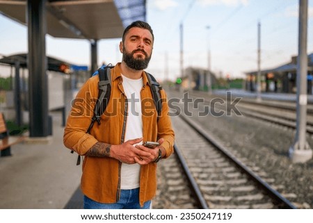 Adult man is standing at railway station and waiting for arrival of train.