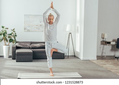 Adult Man Standing In Tree Pose On Yoga Mat At Home