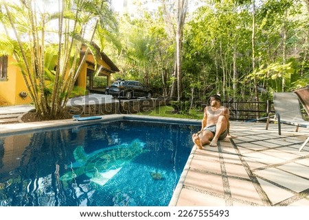 adult man in a swimsuit vacationing in a beach house with a pool in the middle of the tropical forest