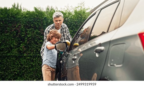 Adult man teaches pre-adolescent son right washing car at backyard on sunny day. Father and pre-teenage boy are using sponges and cleaning auto outdoor near home. Happy family concept. - Powered by Shutterstock