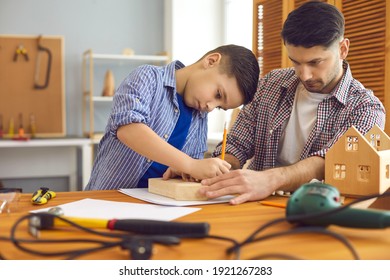 Adult Man Teaching Kid To Make Wooden Toys. Concentrated Little Child And His Father Building House Models At Home. Dad And Son Working With Wood At Carpenter's Workshop As Part Of School DIY Project