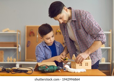 Adult Man Teaching Little Boy To Work With Wood. Serious Child And Father Measuring Wooden House With Tape. Concentrated Dad And Son Making Toys At Carpenter's Workshop As Part Of DIY Homework Project