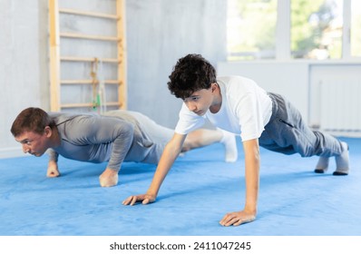 Adult man and teenage boy doing abdominal exercises in gym - Powered by Shutterstock