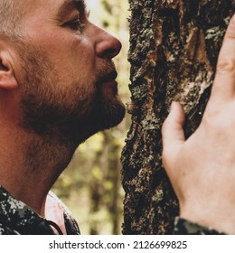 Adult man touches a huge tree, sniffs the bark and hugs the trunk. An adult man enjoys being alone with nature in the forest. The concept of nature conservation, forests, ecology. Human and nature.