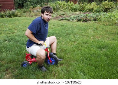 Adult Man Tying To Ride On A Small Tricycle