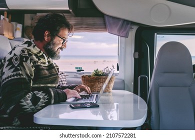 Adult Man Use Laptop Computer To Work Inside Camper Van With Roaming Phone Connection. Concept Of Modern People Lifestyle In Smart Working Or Travel Digital Nomad Freedom