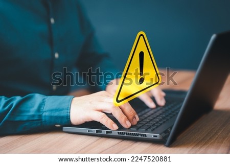 Adult man using computer laptop with triangle caution warning sign for notification error. Computer virus detected, personal data protection, network security and maintenance concept.
