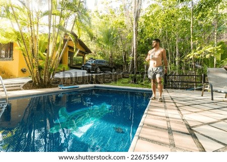 adult man walking with a coffee in a beach house with pool in the middle of the tropical forest