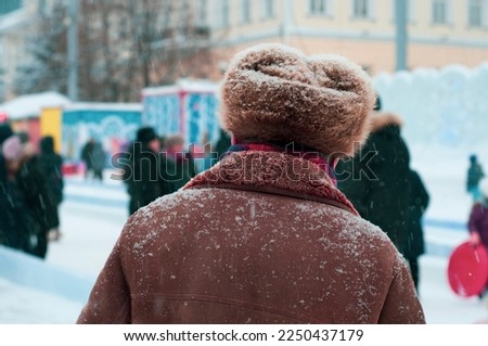 An adult man in a warm fur hat stands on the street in winter, under the falling snow. Soviet, Russian hat. Fur hat, Wool hat. Russian winter Cap