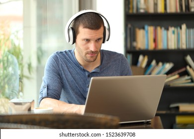 Adult man wearing headphones using a laptop e-learning in a coffee shop or home - Shutterstock ID 1523639708