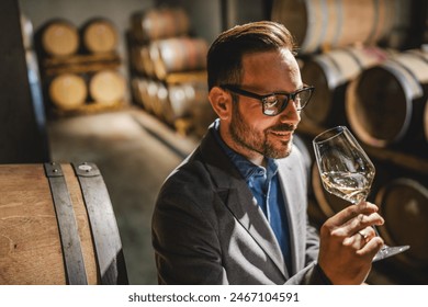 Adult man winemaker hold glass and drink wine stand between the barrels in the cellar check process of make white wine - Powered by Shutterstock