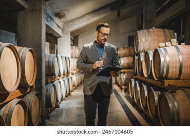 Adult man winemaker hold glass and drink wine stand between the barrels in the cellar check process of make white wine - Powered by Shutterstock