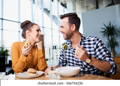 Adult man and woman in casual clothes eating in cafe and smiling to each other