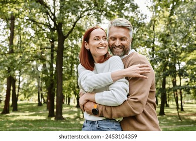 An adult man and woman in casual clothing hug affectionately in a park. - Powered by Shutterstock