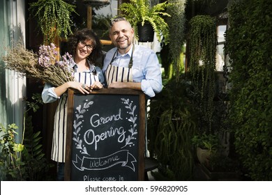 Adult Man And Woman Standing With Grand Opening Sign