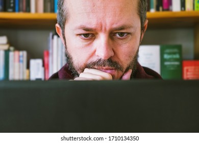 Adult Man Working From Home Office. Bearded Man Working Online From Home On Computer Laptop, Book Shelves Behind Him. Face Expression, Shock, Surprise, Confusion. Close Up.