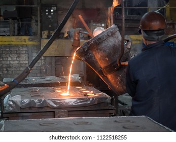 Adult Mens In Protective Clothing And Helmets Are In The Foundry And Pour Liquid Metal Into The Foundry Models