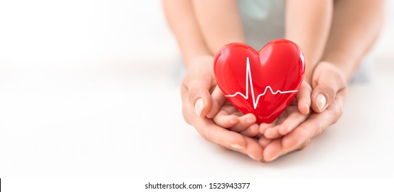 An adult, mother and child hold a red heart in their hands. Concept for charity, health insurance, love, international cardiology day.