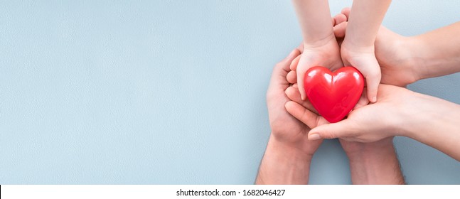 An adult, mother, father and child hold a red heart in their hands. Concept for charity, health insurance, love, international cardiology day.