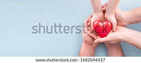 An adult, mother, father and child hold a red heart in their hands. Concept for charity, health insurance, love, international cardiology day.