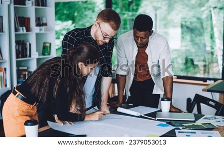 Adult multiethnic colleagues intently working with draft in cozy open space office