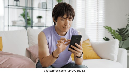 Adult people asia single LGBT gay man sitting at home sofa looking at dating game tinder app on mobile phone. Relax smile choose lover enjoy playing right swipe to find love couple match flirt chat. - Powered by Shutterstock