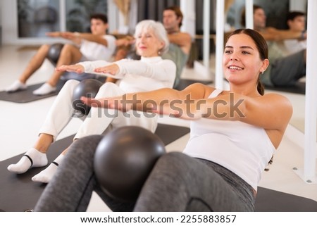 Adult people different ages practicing pilates with ball at group class in yoga studio