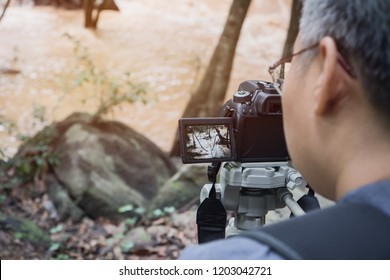 Adult People Video Journalist Or Reporter Take Photo Or Video At Stream River Fast Landscape With Tree Forest, Rocks Beautiful Scenery For Peaceful In Spring Rain Forest In Thailand.