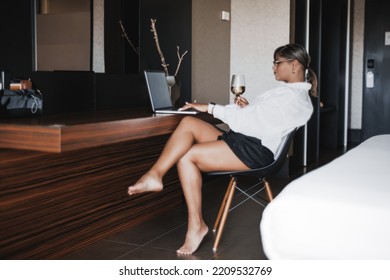 An Adult Plus-size Hispanic Woman Is Pausing The Series Which She Is Watching On The Screen Of Her Laptop While Sitting In A Hotel Room During Her Vacation With A Glass Of White Wine In Her Hand