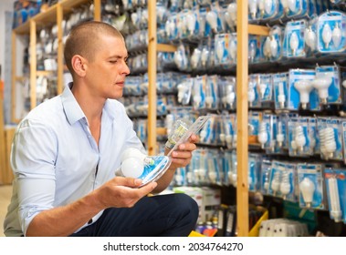 Adult positive man visiting store of household goods in search of energy efficient light bulbs - Shutterstock ID 2034764270