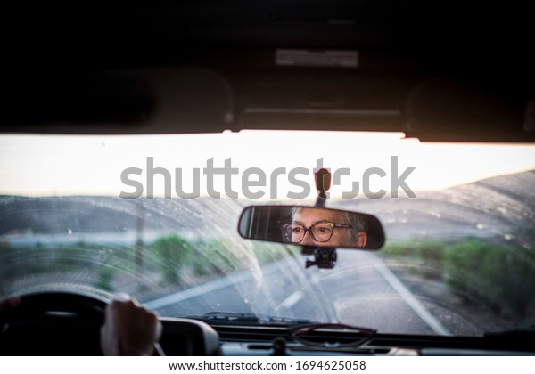 Adult senior woman driving a car\
looking at the road and using eyeglasses to see better - concept of\
drive vehicle -  insurance and travel old mature\
people