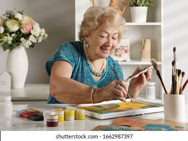 Adult senior woman paints a picture in her studio. Hand made art crafts theme