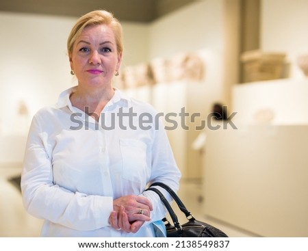 Adult senior woman visitor looking at exposition of artworks in historical museum