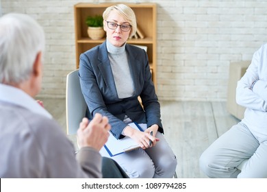 Adult Serious Woman Listening To Problems Of Elderly People In Assisted Living Center Taking Care Of Patients. 