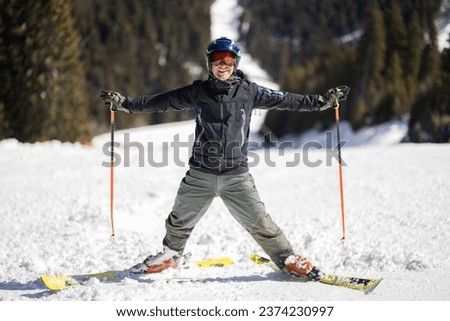 Adult skier standing on slopes in a mountain ski resort. Man posing outdoors on a sunny winter day.