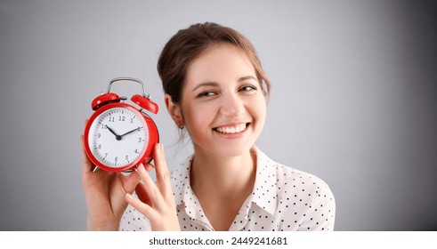 Adult smiling caucasian woman hold red alarm clock on gray background. - Powered by Shutterstock