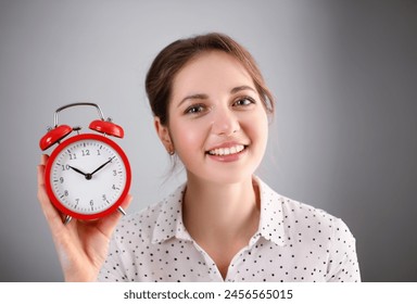 Adult smiling caucasian woman hold red alarm clock on gray background. - Powered by Shutterstock