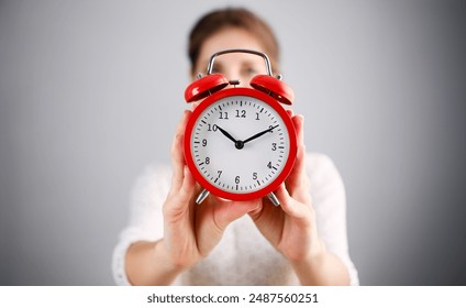 Adult smiling caucasian woman hold red alarm clock on gray background. - Powered by Shutterstock