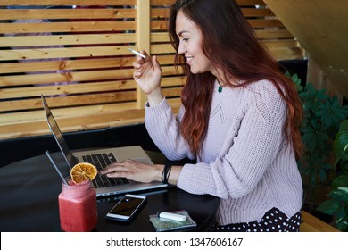 Adult Smiling Female Smoking Marijuana Joint And Working On A Laptop At The Cafe