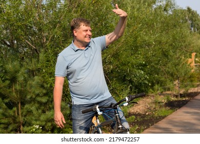 An Adult Smiling Man On A Bicycle Calls A Friend With A Hand Gesture.