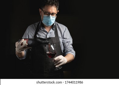 Adult Sommelier Wearing A Coronavirus Face Mask Pours Red Wine Into A Glass. Reopening Concept In Phase Two After The Lockdown.