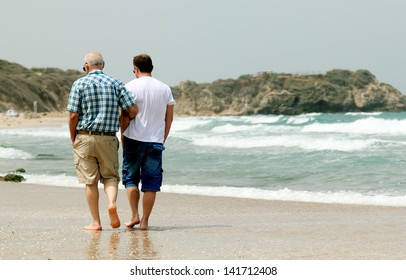 Adult Son And Father Walking Together On The Beach