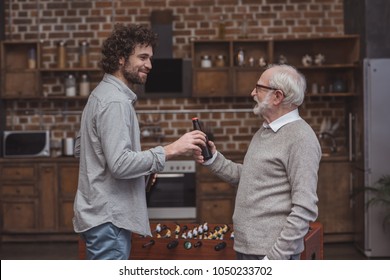 Adult Son Giving Senior Father Bottle Of Beer At Home