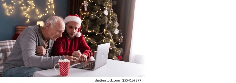 Adult son and his retired father shopping online using credit card and laptop computer sitting on sofa on christmas eve together. Banner. Copy space - Powered by Shutterstock