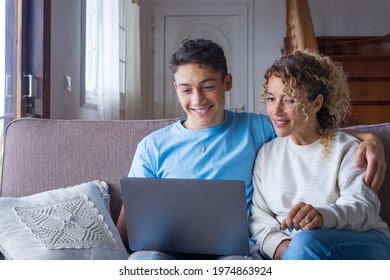Adult son and middle-aged 40s mother sitting on couch in cozy living room holding on lap notebook laughing on funny comedy movie, enjoy on-line amusements websites, internet virtual fun online concept - Shutterstock ID 1974863924