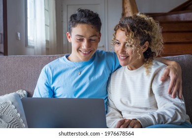 Adult son and middle-aged 40s mother sitting on couch in cozy living room holding on lap notebook laughing on funny comedy movie, enjoy on-line amusements websites, internet virtual fun online concept - Shutterstock ID 1976678564